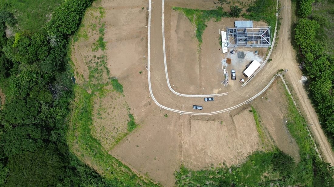 Aerial view of graded building platforms and the curved access road, dense forest along the left edge